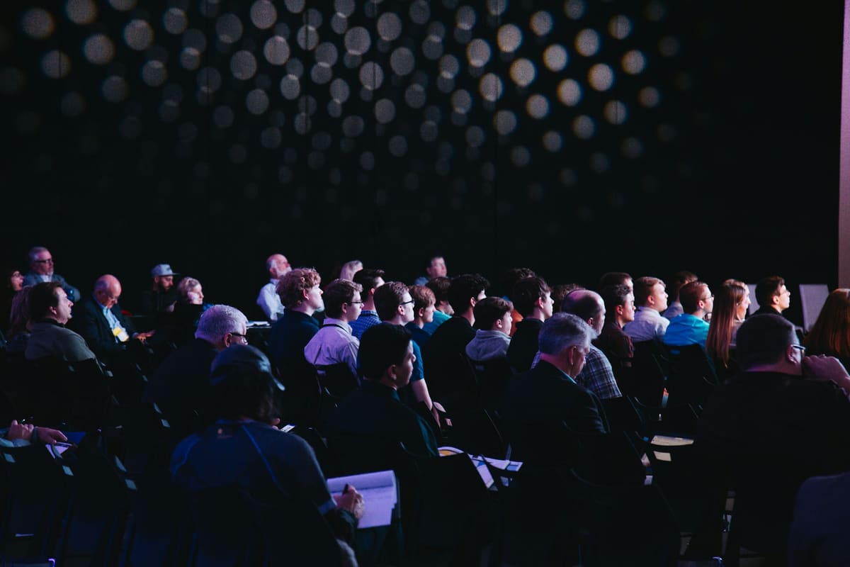 An audience seated and standing within a large conference exhibition space.